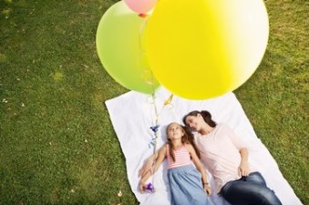 Mother and daughter lying on blanket holding balloons, high angle